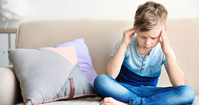 Little boy suffering from headache while sitting on couch at hom